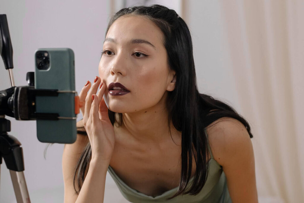 Mujer en frente de su celular aplicando productos de belleza